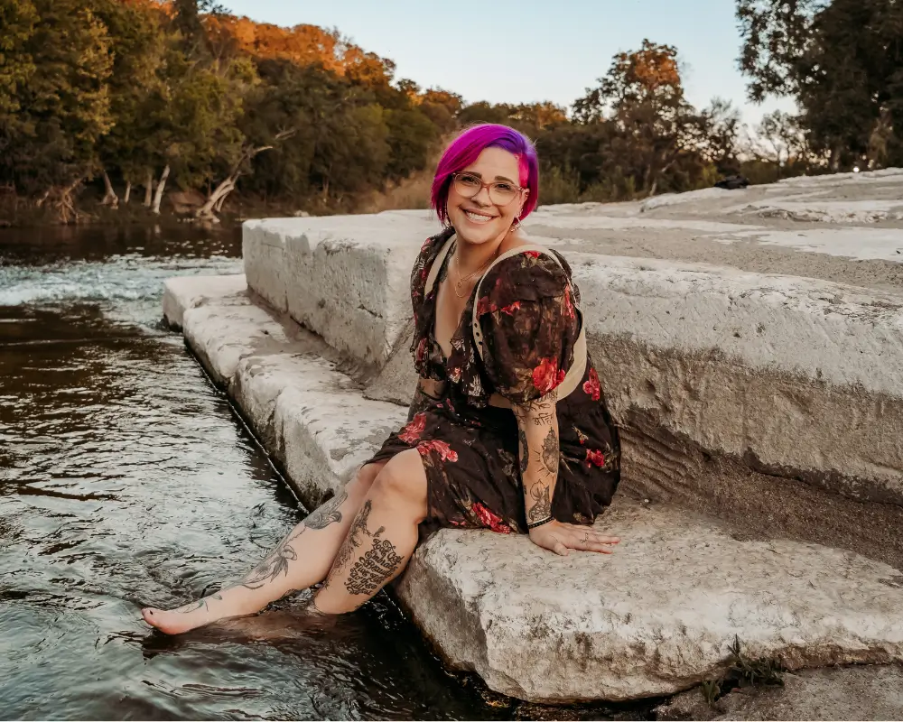 dr. emma j. church with feet dangling in a river pink hair